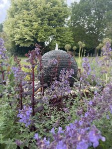 A slate ball water feature is surrounded by garden cottage style planting in tones of purple and mauve