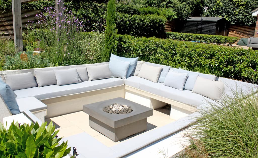 A sunken seating area with contemporary gas fire pit. The fitted seating is decorated with inviting cushions
