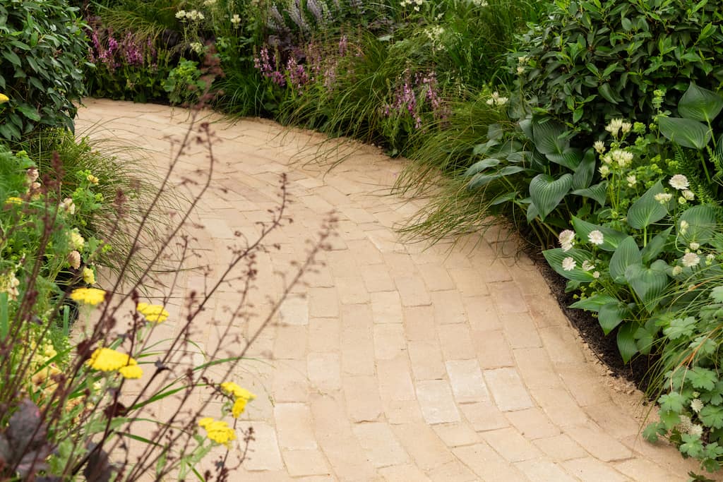A garden path constructed from warm coloured clay pavers and with a touch of sparkle through the glitter grout undulates through planting areas