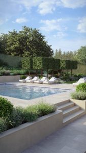 A view across a modern garden which includes a set of steps leading to a swimming pool area. Sun loungers can be seen in the mid ground. In the background, a double row of box head pleached trees can be seen with natural trees to the rear of these.